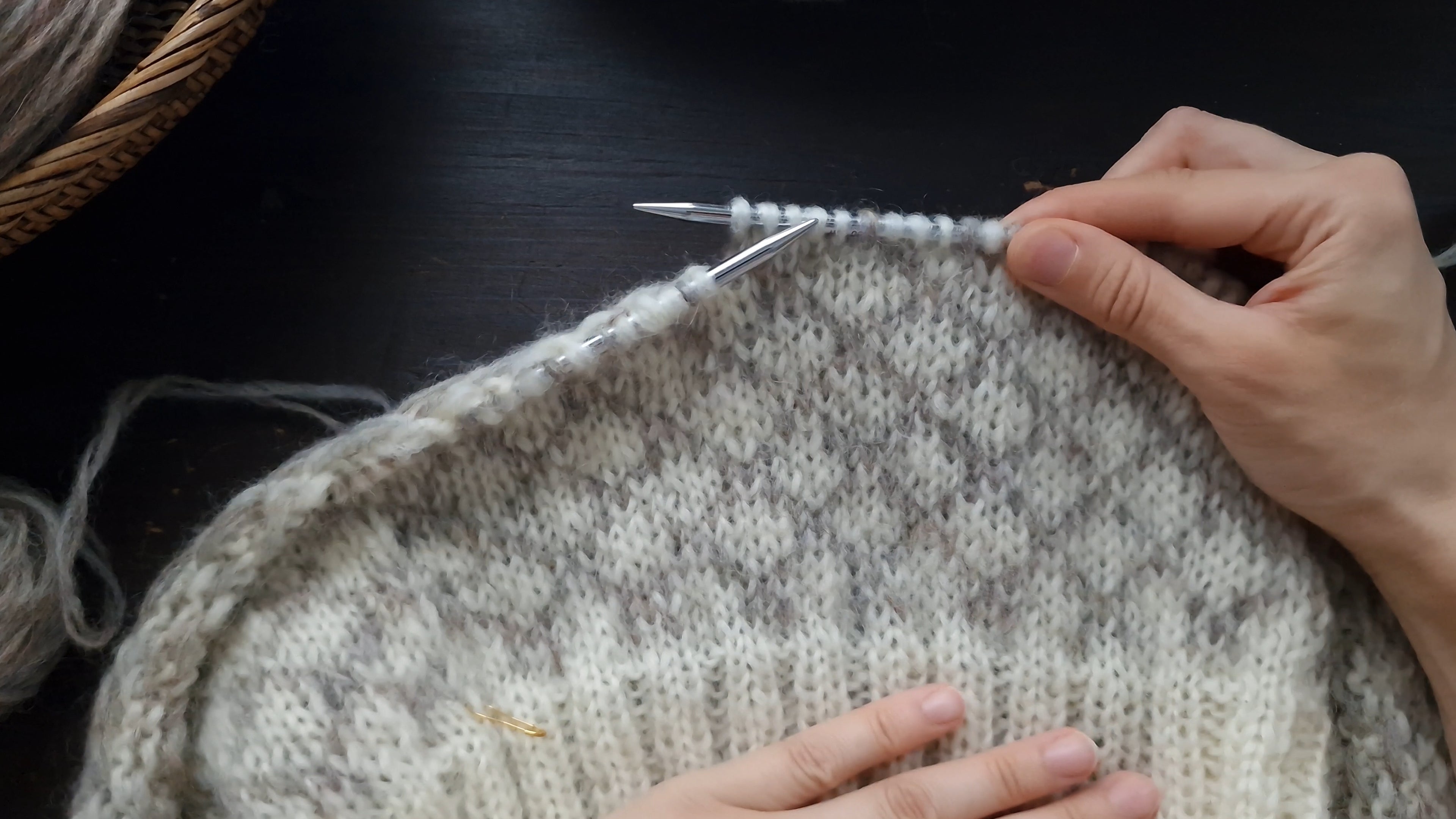 Hands placed on stranded colourwork knitting project sweater with unspun wool yarn on circular needles
