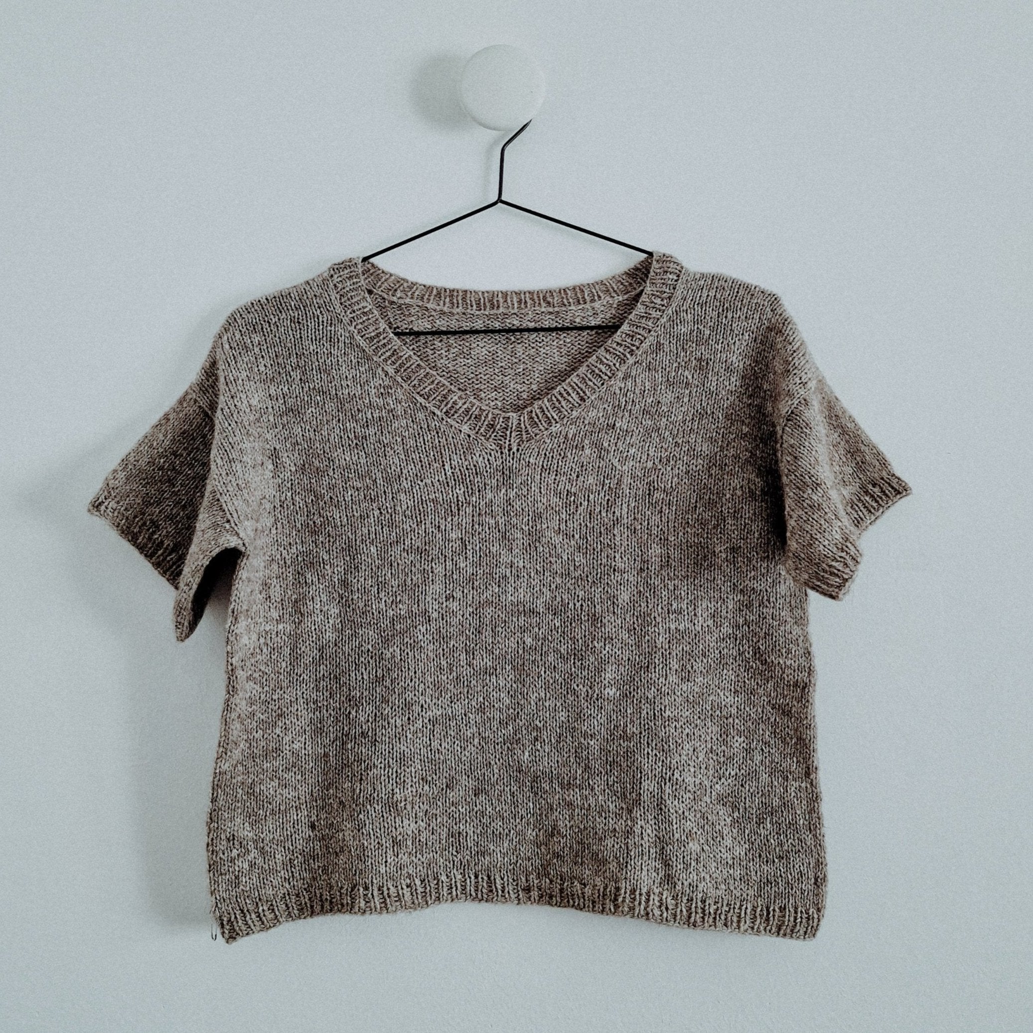 Beige ribbed knit sweater with V-neckline and short sleeves displayed on hanger.