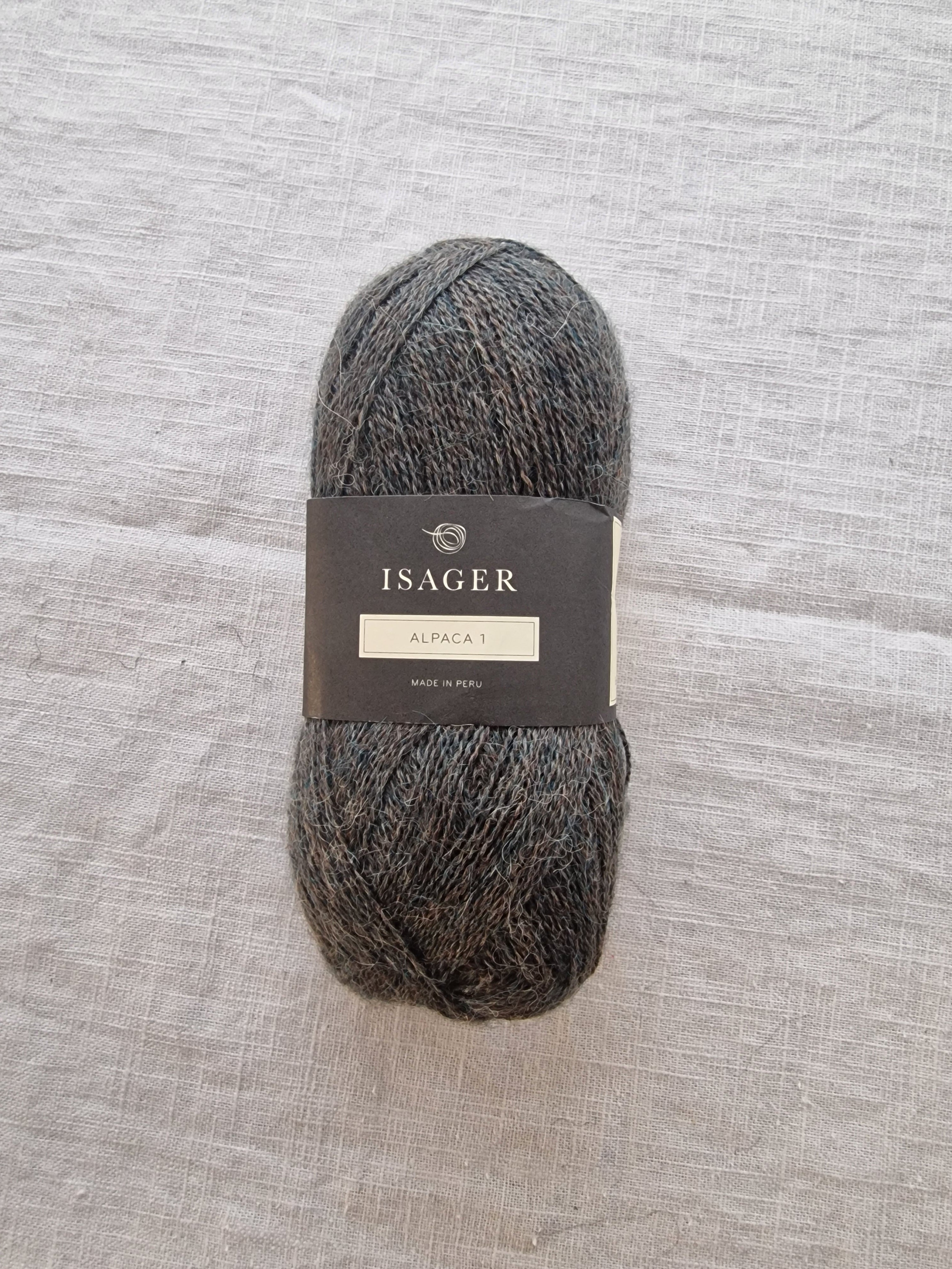 Skein of dark grey alpaca lace weight yarn with label displayed on neutral linen background.