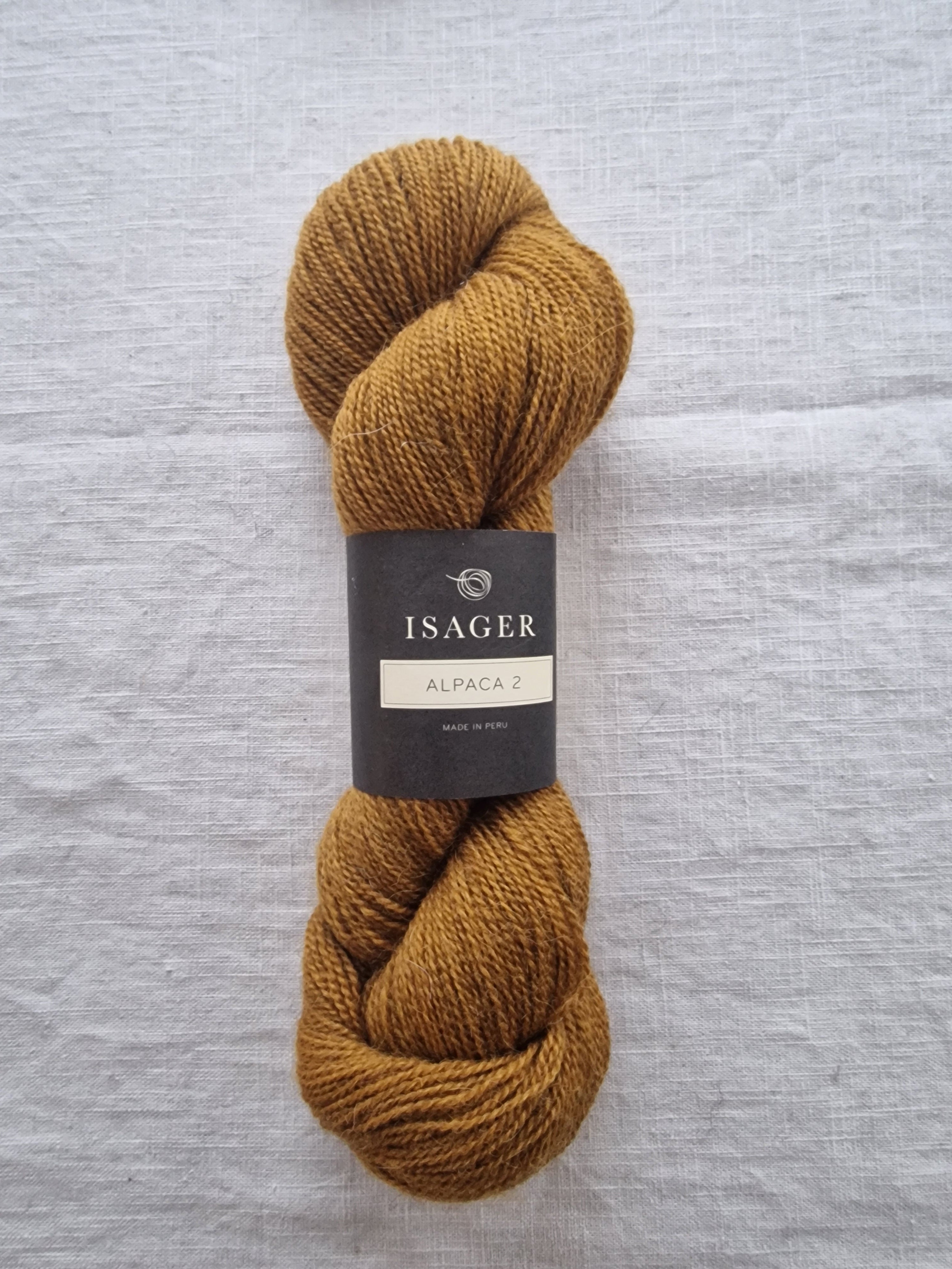 Mustard yellow skein of yarn with a label on a light gray background