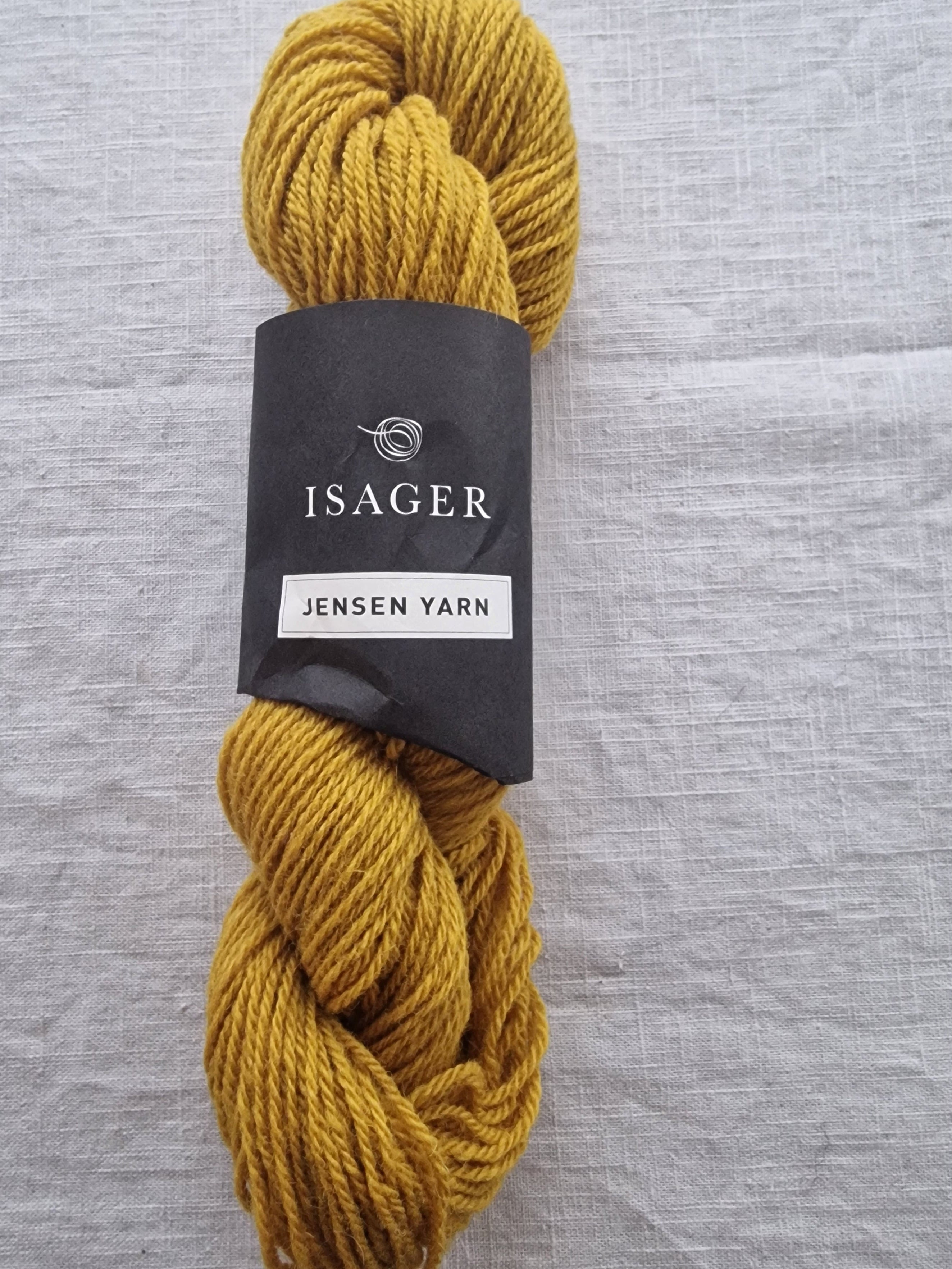 Mustard yellow sport weight wool yarn skein with twisted texture displayed on neutral linen background.