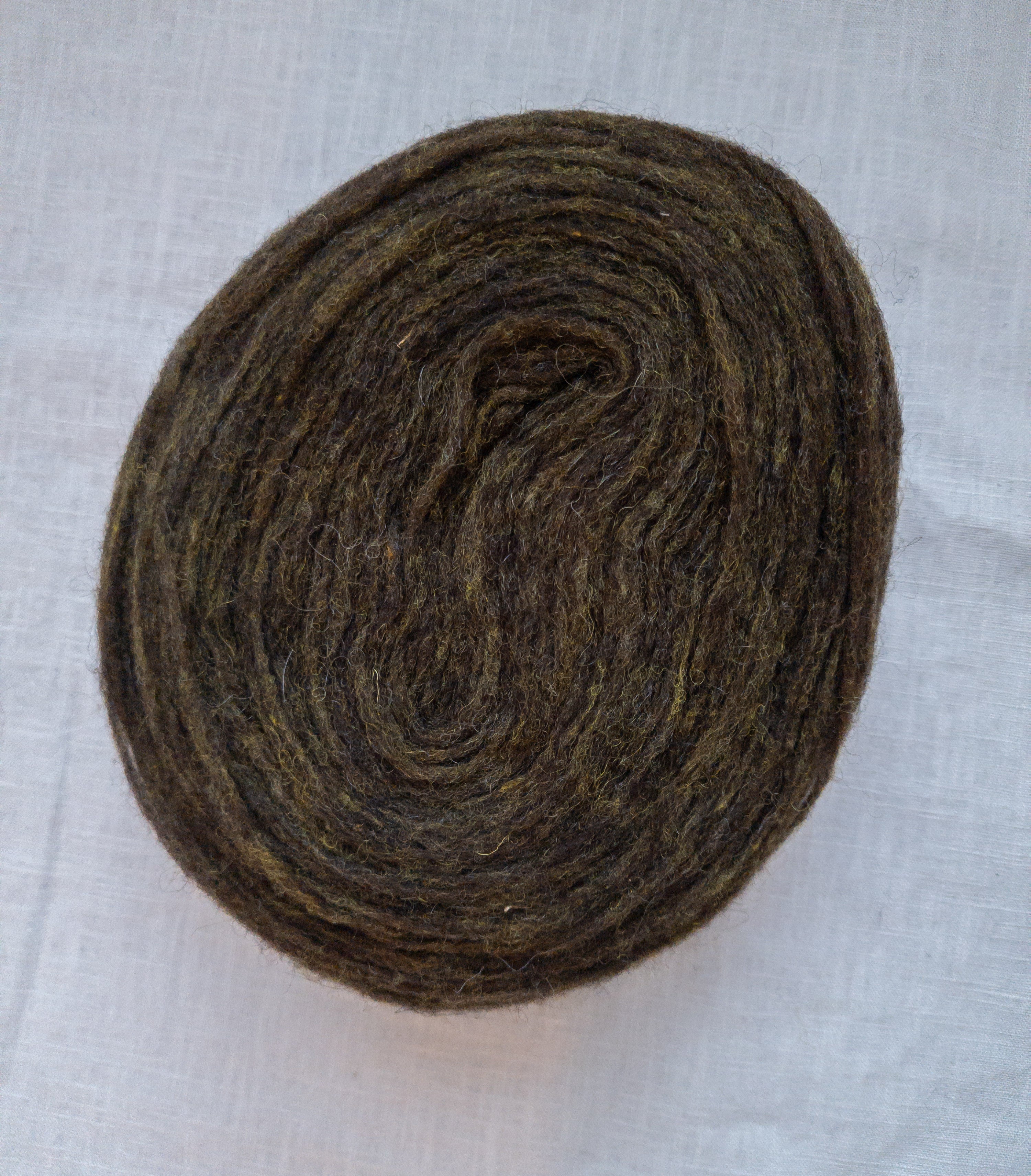 Cake of unspun Swedish wool yarn in dark moss green olive color with natural heathered texture.