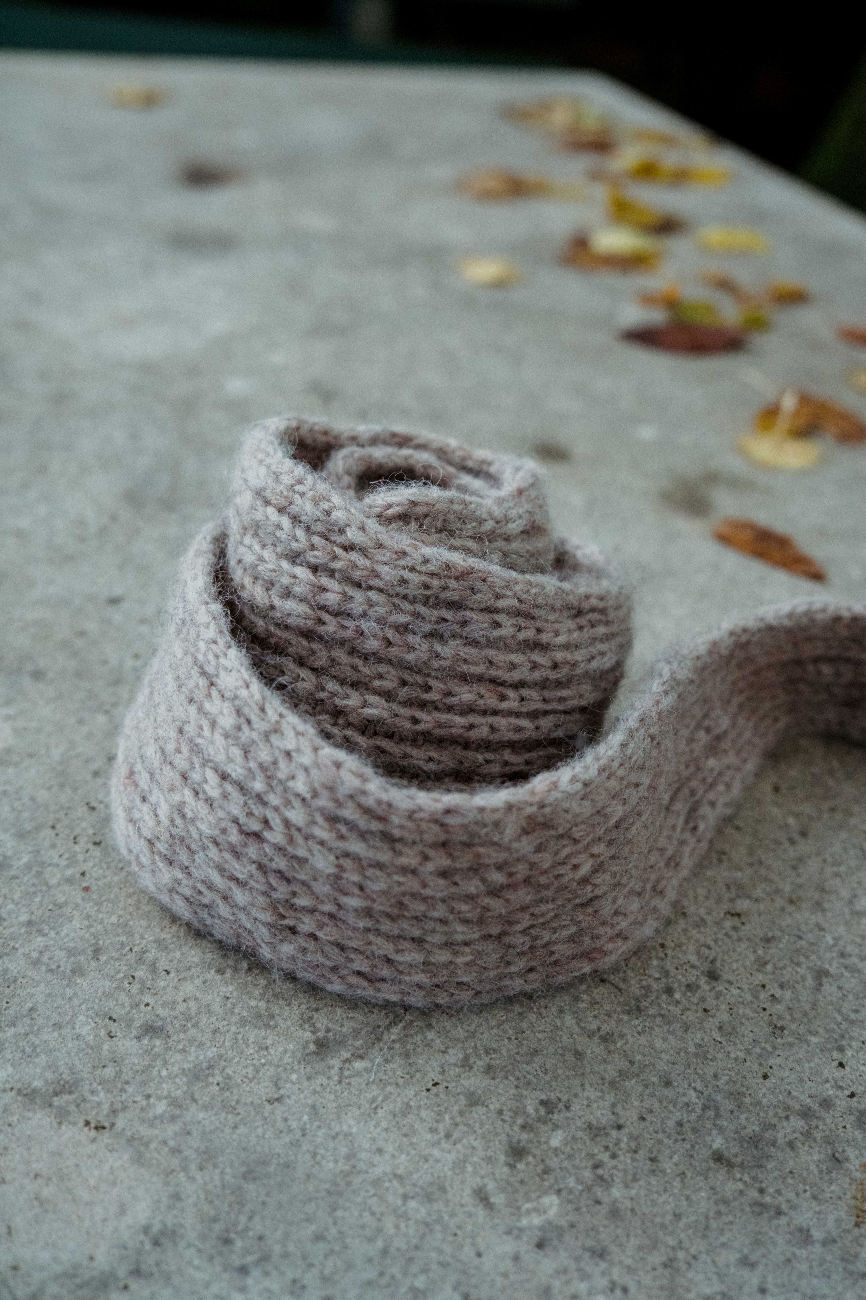Season's End Shawl, handknit in half-brioche with I-cord edges from unspun Nutiden yarn by Höner och Eir, rolled on a concrete table amid fall ambiance.