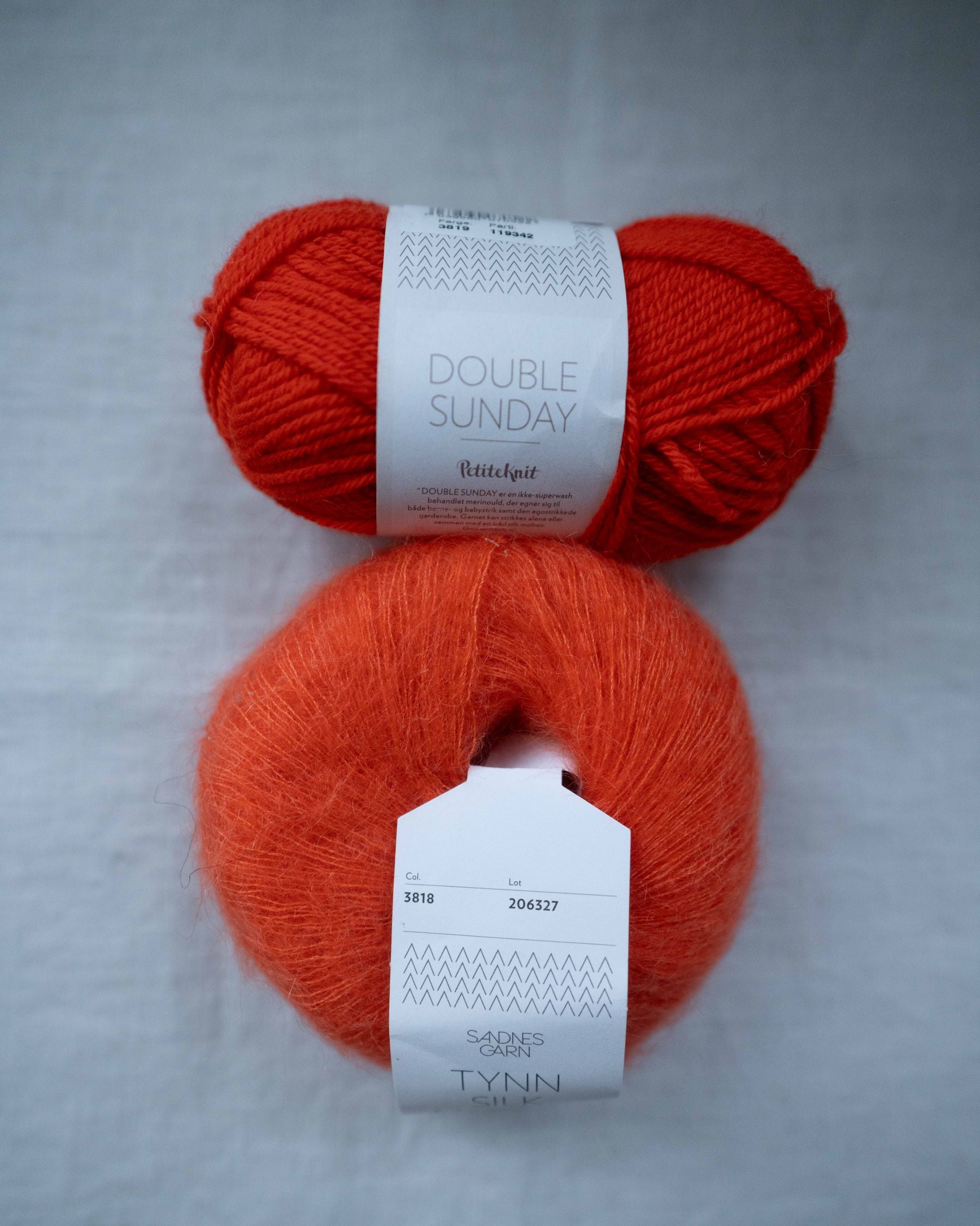 Bundle of Double Sunday wool yarn and Tynn Silk Mohair in vibrant orange-red tones for knitting projects.