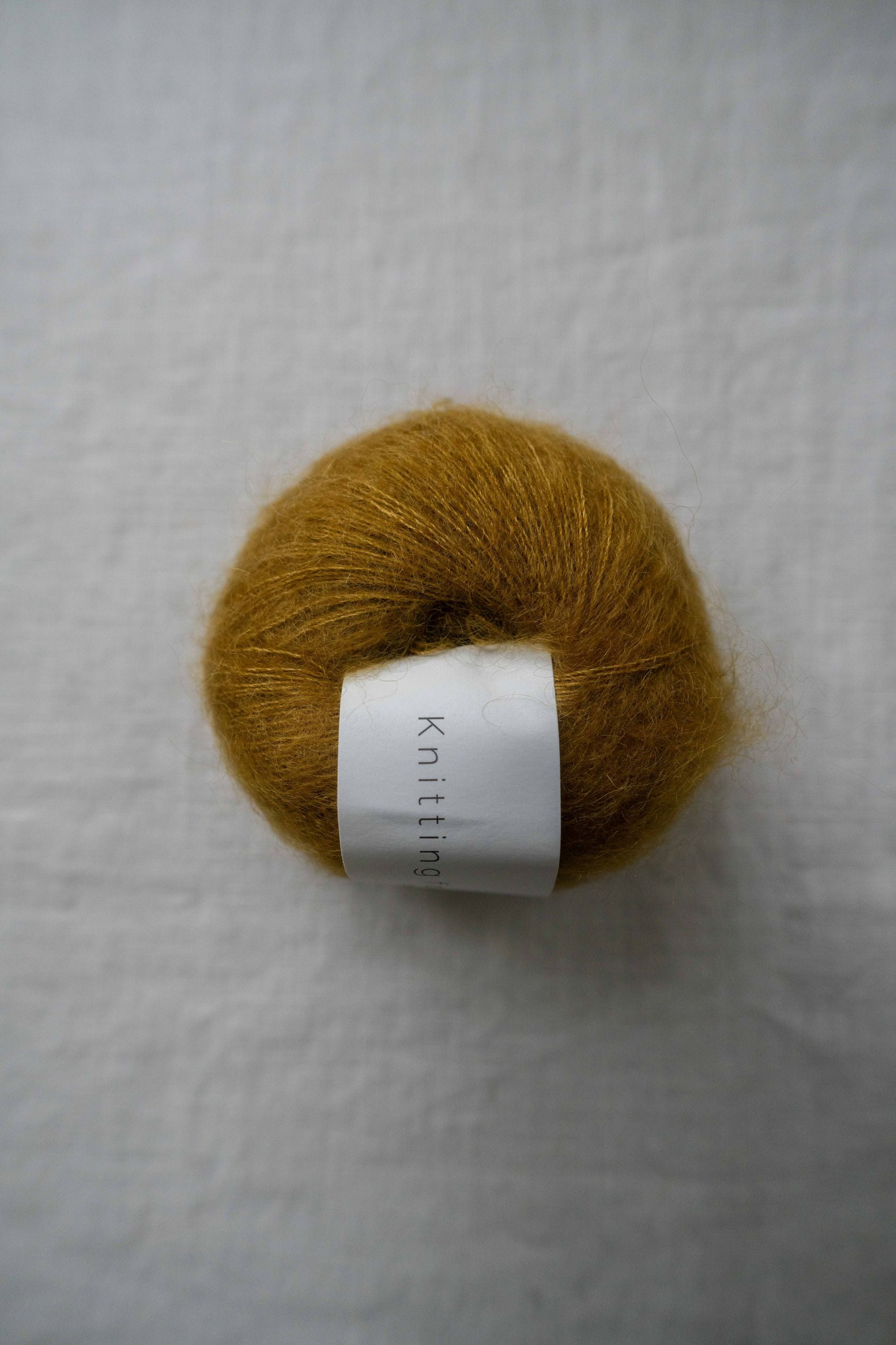Soft golden amber mohair yarn ball with fuzzy texture and white knitting label on neutral linen background.