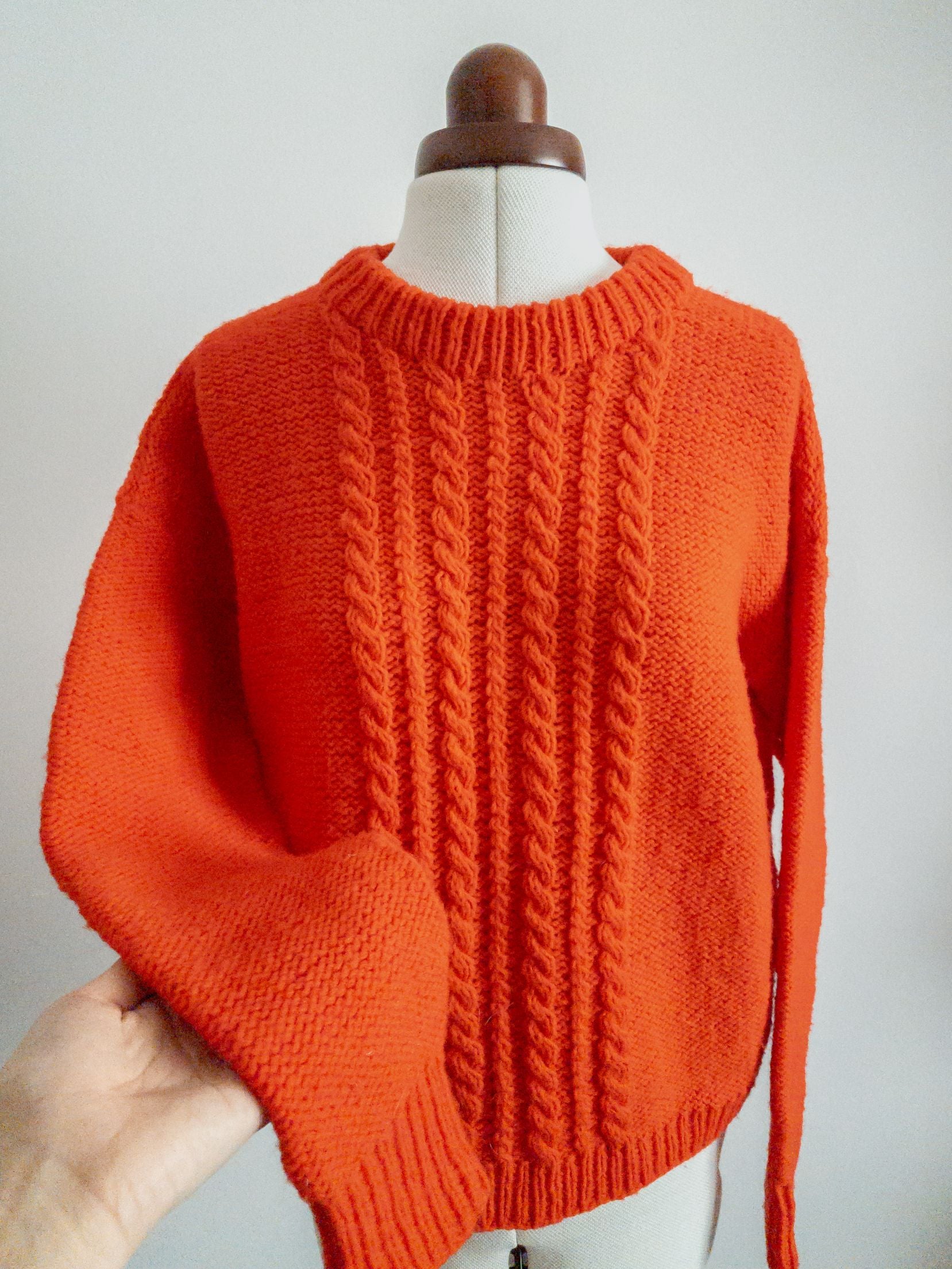 Bright orange cable knit sweater with crew neckline displayed on dress form mannequin.