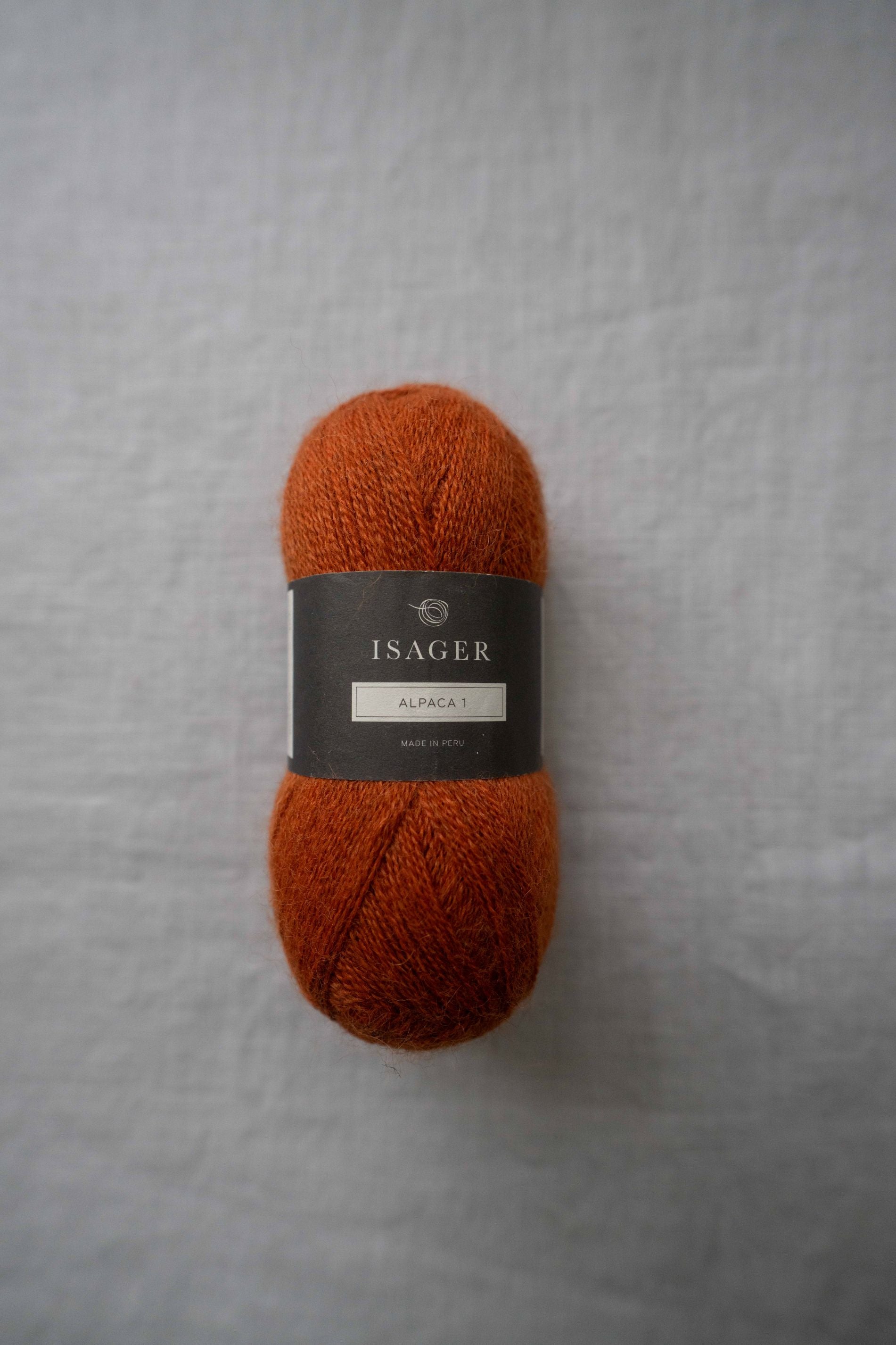 Skein of burnt orange alpaca yarn with a soft, fine texture displayed on grey linen background.