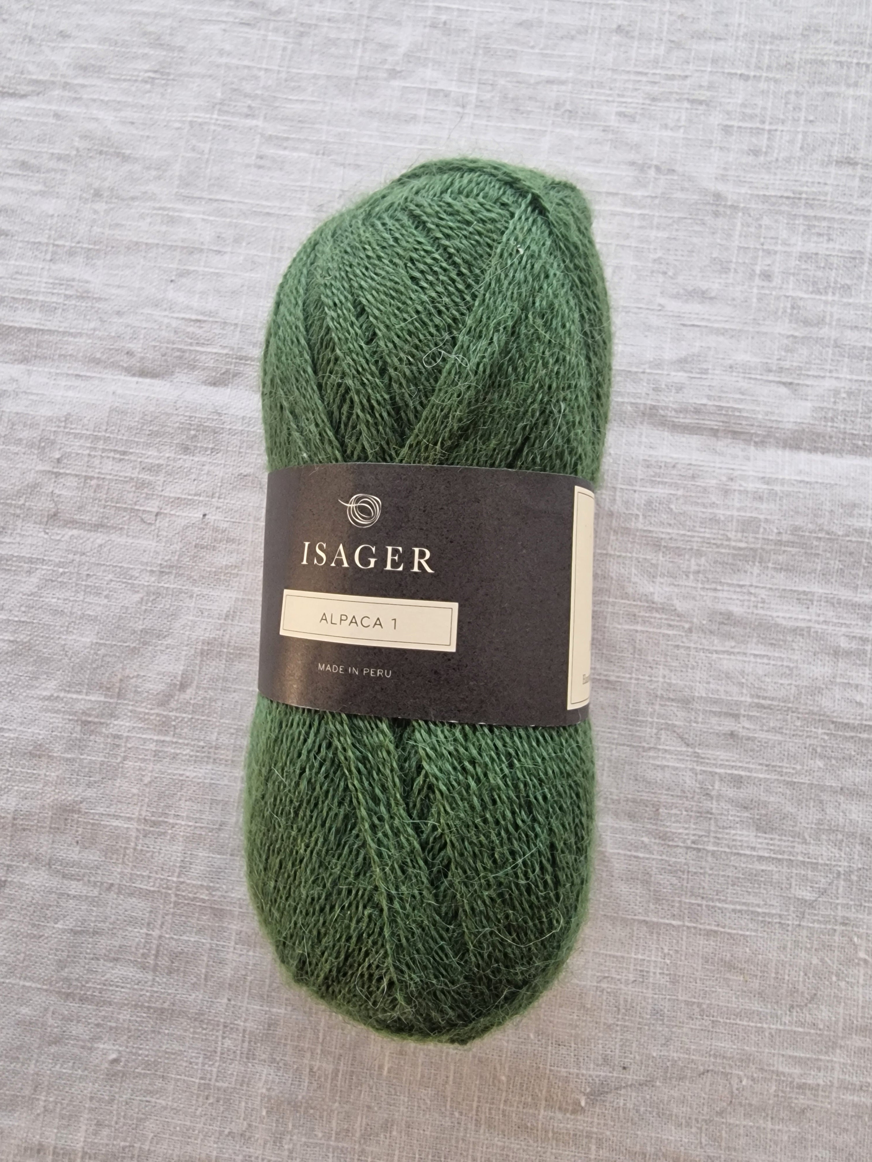 Skein of soft green alpaca yarn with a fine, delicate texture displayed on linen fabric.