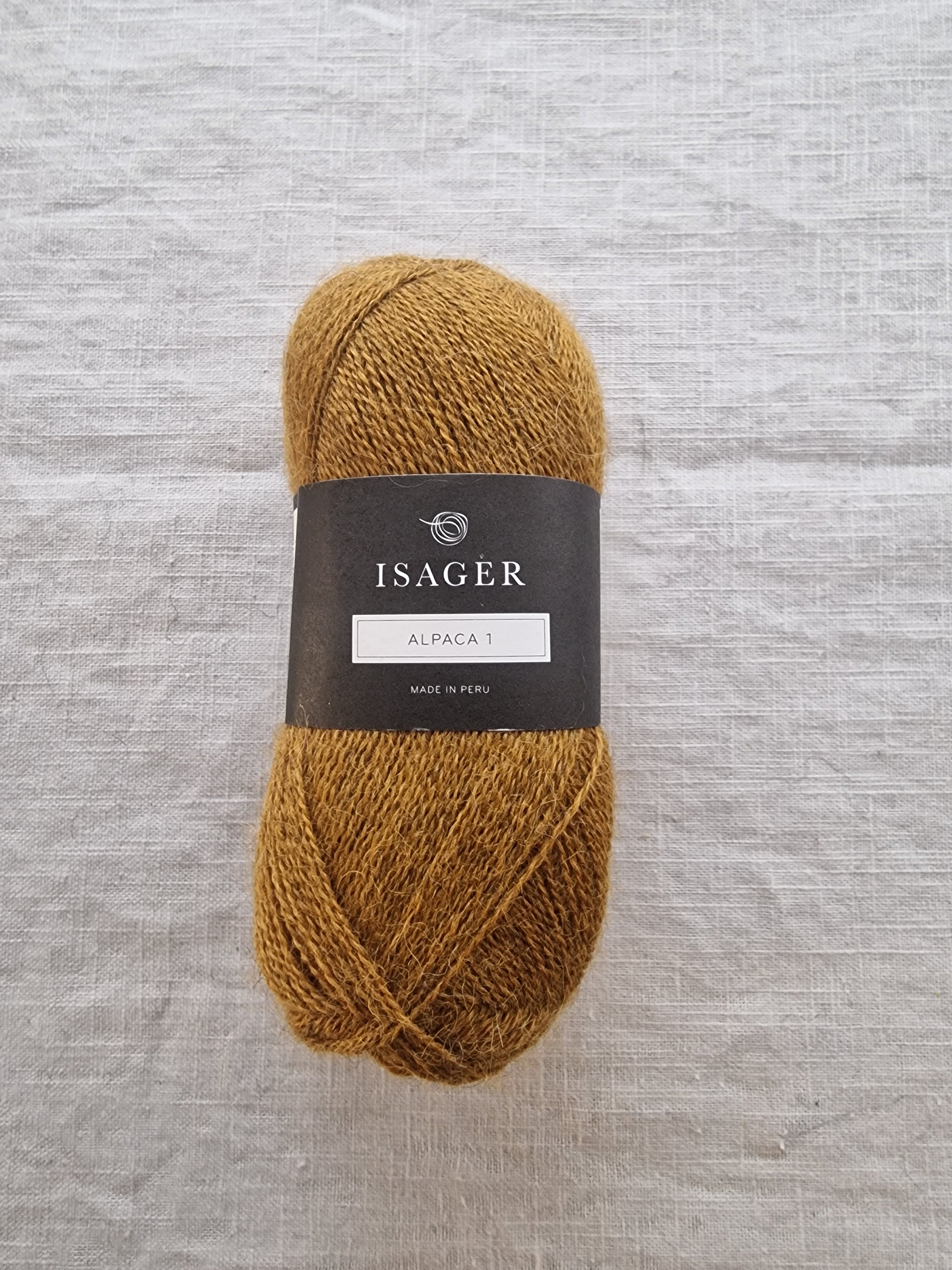 A skein of golden mustard alpaca yarn with a soft, lightweight texture displayed on linen fabric.