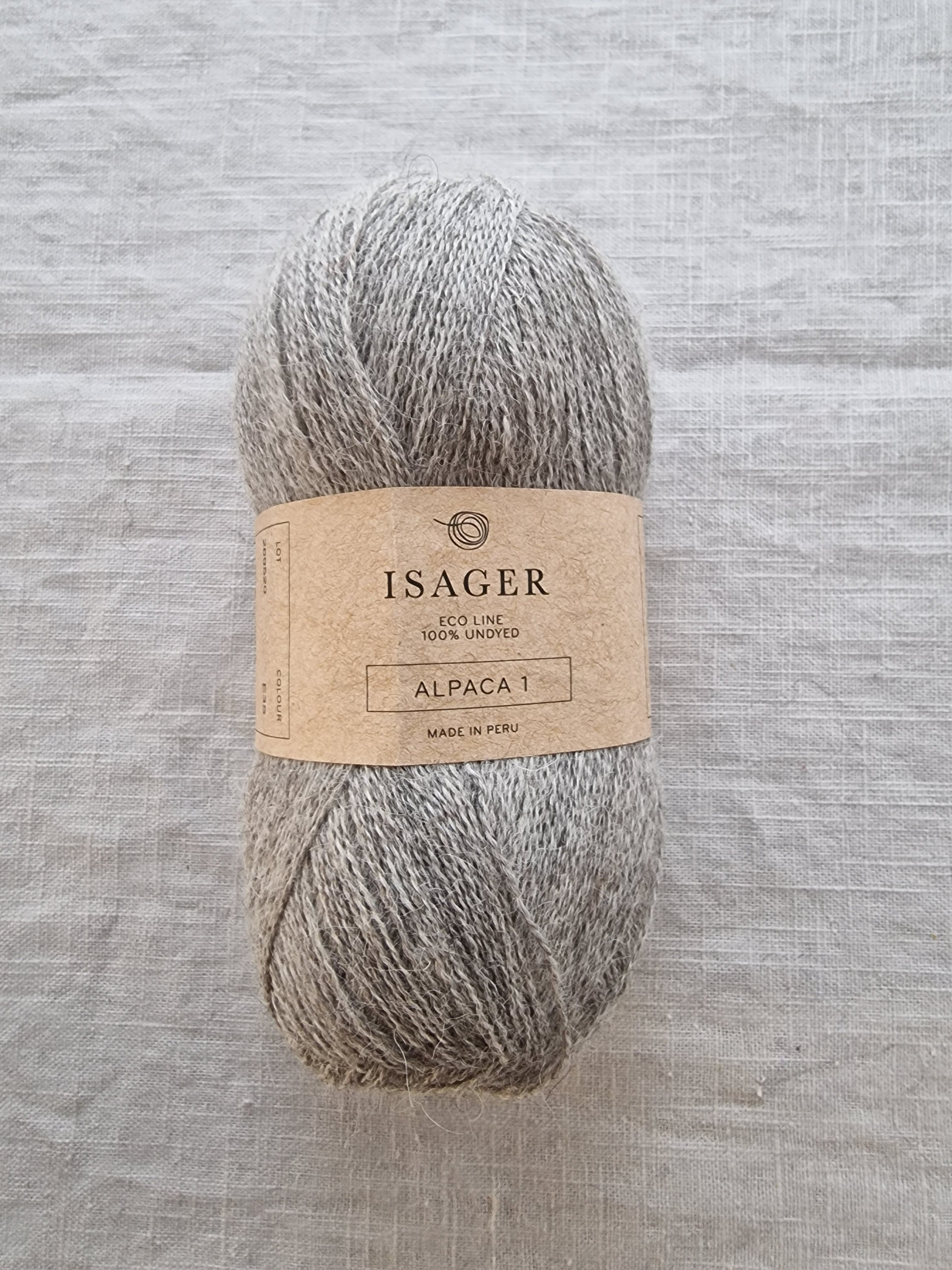 Skein of undyed grey alpaca yarn with natural heathered texture and eco-friendly kraft paper label.