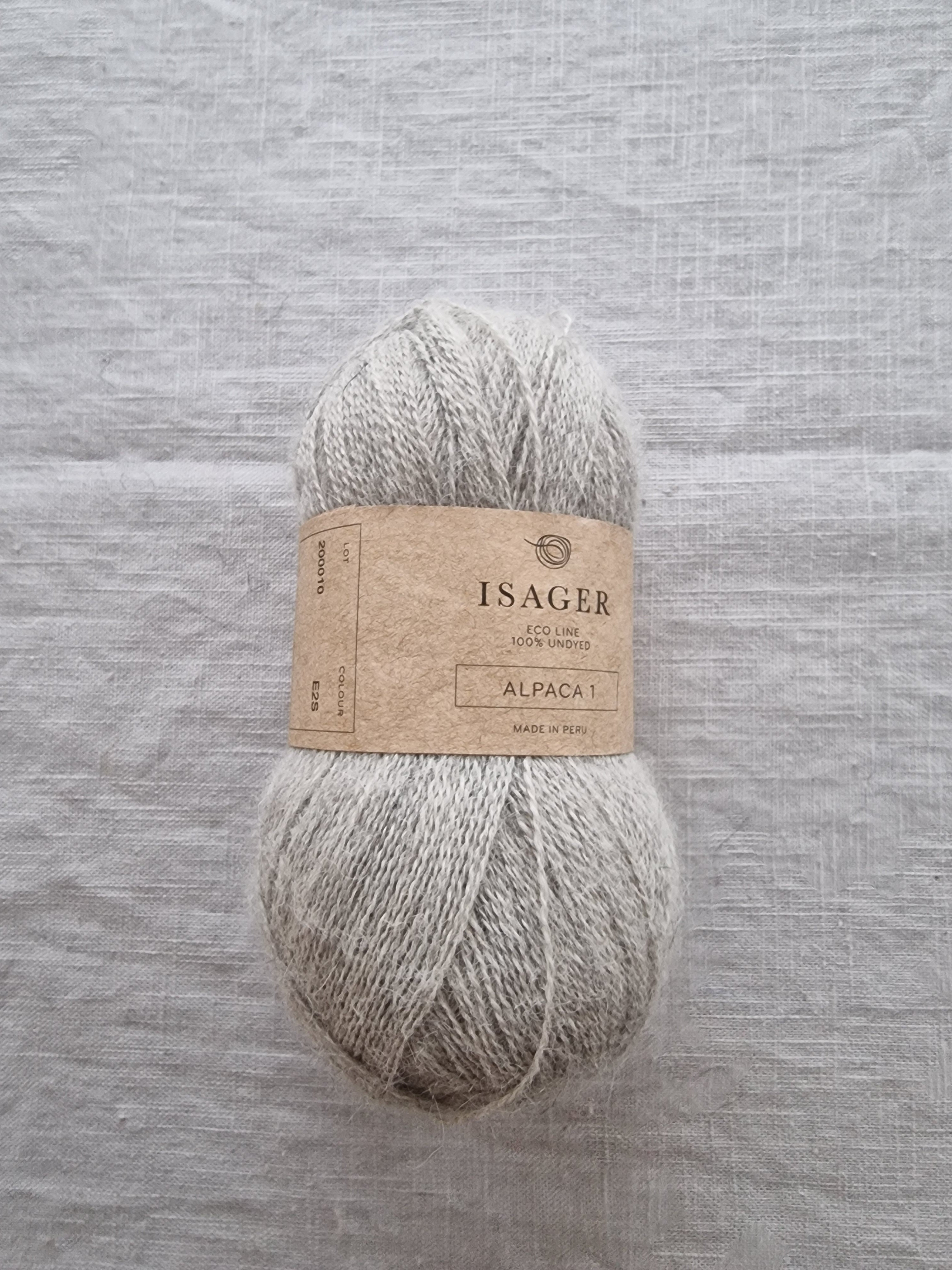Skein of undyed grey alpaca yarn with natural heathered texture displayed on linen fabric background.