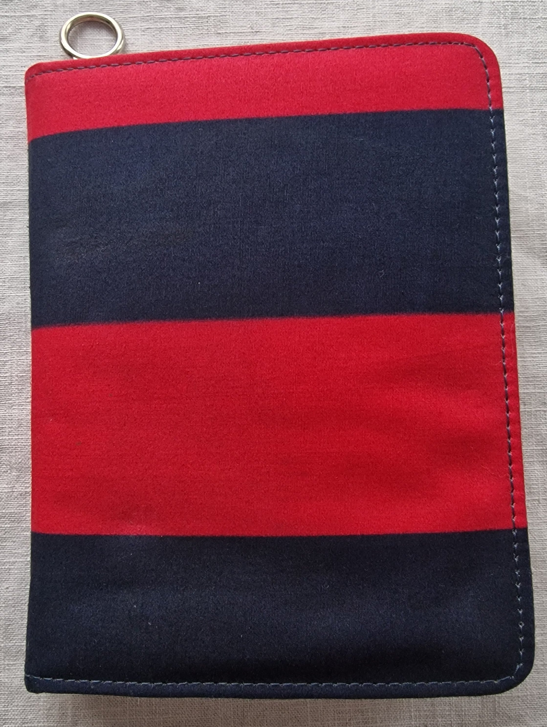 Red and navy blue striped knit pouch with metal ring detail and visible stitching on edges.
