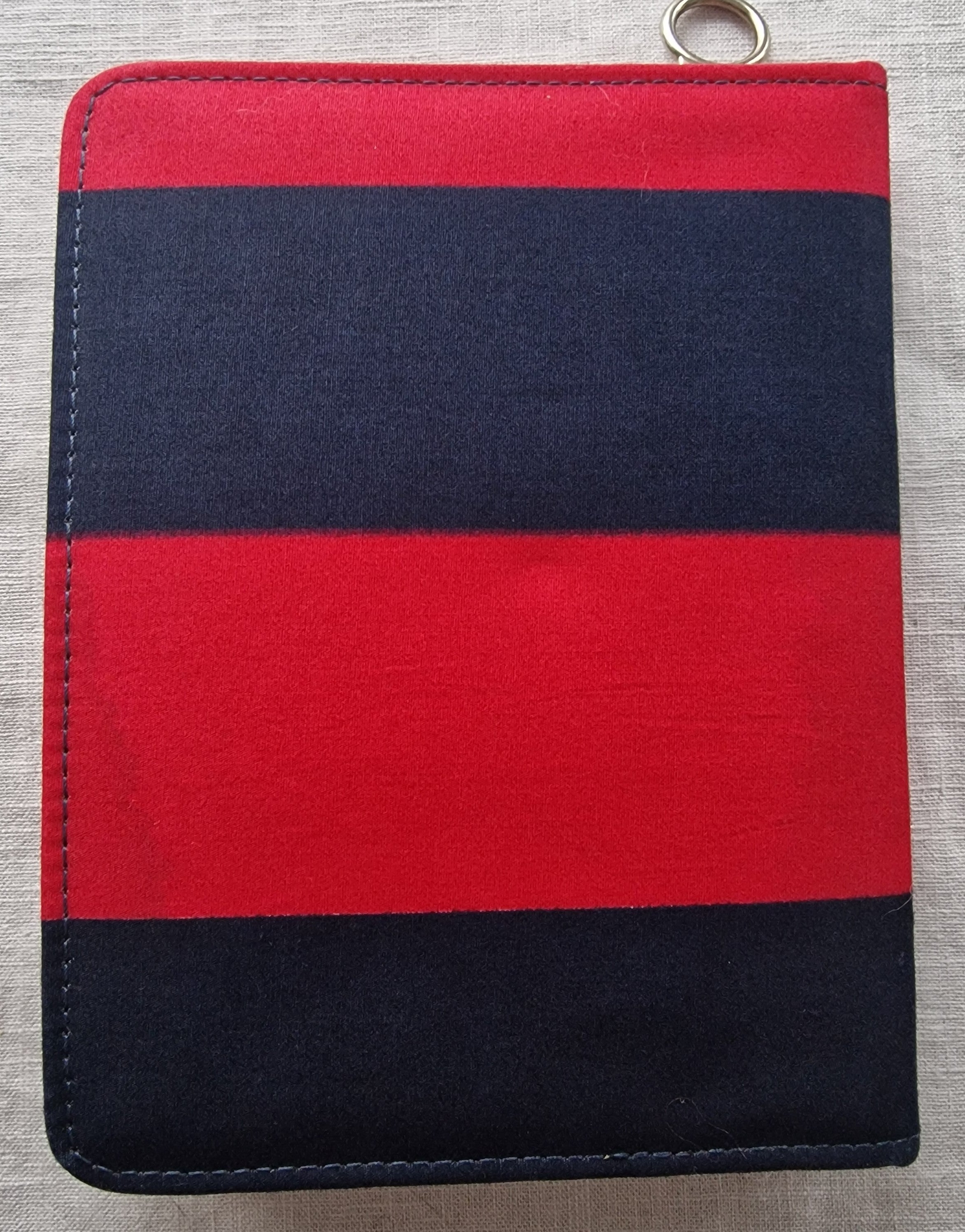 Red and navy blue striped knit pouch with metal ring detail, displayed flat on neutral fabric background.